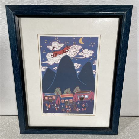 Print copy of "Lunar Eclipse" shows a pig jumping over the mountains in the night sky with a village at the base made by Lee Ngo and has a blue wood frame with white mat